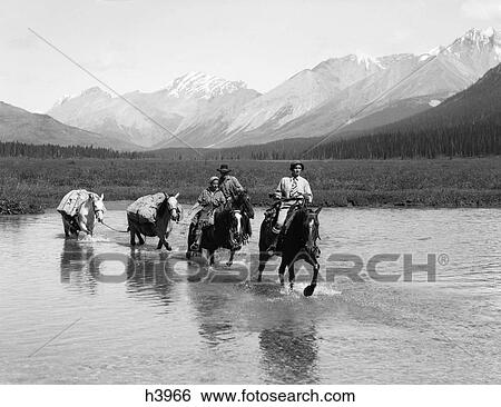 1930S Two Women Man Riding Horseback Through Shallow Water Two Extra Horses Carry Camping Equipment Mountains In Background View Large Photo Image Stock Photograph - 1930S Two Women Man Riding Horseback Through Shallow Water Two Extra Horses Carry Camping Equipment Mountains In Background. Fotosearch