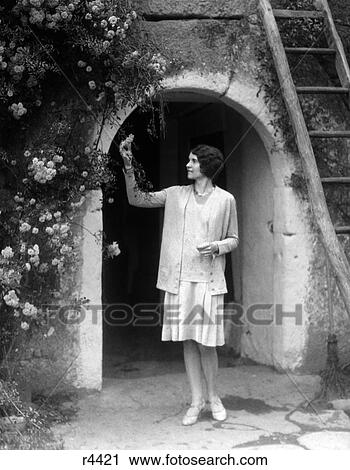 1930S Woman In Flapper Outfit Standing In Front Of Whitewashed Archway With Flowers Picking Bud Brittany France View Large Photo Image Stock Image - 1930S Woman In Flapper Outfit Standing In Front Of Whitewashed Archway With Flowers Picking Bud Brittany France. Fotosearch
