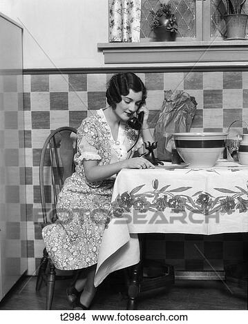 1930S Woman Sitting At Kitchen Table With Table Cloth While Smiling On Phone View Large Photo Image Picture - 1930S Woman Sitting At Kitchen Table With Table Cloth While Smiling On Phone . Fotosearch
