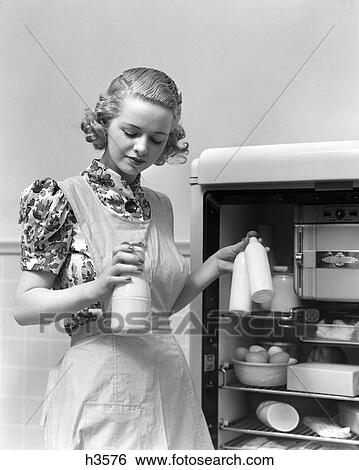 1930S Woman Wearing A White Apron Taking Milk Out Of The Refrigerator View Large Photo Image Stock Photograph - 1930S Woman Wearing A White Apron Taking Milk Out Of The Refrigerator . Fotosearch