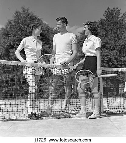 1940 1940S 1950 1950S Two Girls And A Guy Tennis Players Holding Rackets And Tennis Ball Standing Near Net On Court View Large Photo Image Stock Photograph - 1940 1940S 1950 1950S Two Girls And A Guy Tennis Players Holding Rackets And Tennis Ball Standing Near Net On Court . Fotosearch