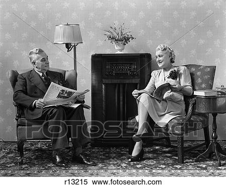 Stock Photography - 1940 1940S Elder Couple Sitting In Living Room Reading Newspaper And Magazine Listening To Radio . Fotosearch