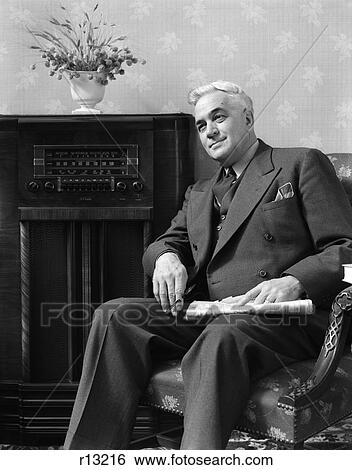 1940 1940S Elder Man Sitting In Living Room Holding Newspaper Listening To Radio View Large Photo Image Stock Photograph - 1940 1940S Elder Man Sitting In Living Room Holding Newspaper Listening To Radio . Fotosearch