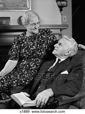 1940 1940S Elderly Couple Sitting In Chair Looking At Each Other View Large Photo Image Stock Photo - 1940 1940S Elderly Couple Sitting In Chair Looking At Each Other . Fotosearch