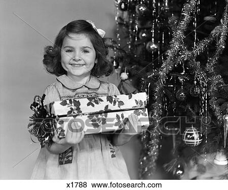 1940 1940S Little Girl Standing Near Christmas Tree Holding A Wrapped Present Smiling View Large Photo Image Stock Photo - 1940 1940S Little Girl Standing Near Christmas Tree Holding A Wrapped Present Smiling . Fotosearch
