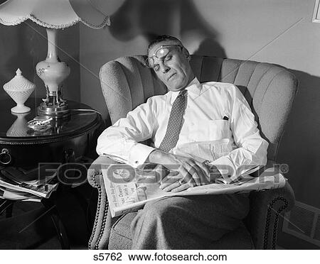 Stock Image - 1940 1940S Man Fell Asleep While Reading Newspaper In Chair Glasses On Forehead . Fotosearch
