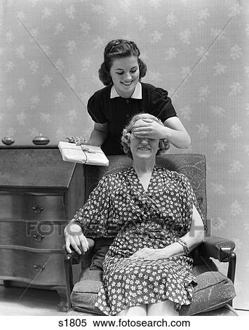 Stock Photography - 1940 1940S Two Women Mother Daughter Daughter'S Hand Covering Mother'S Eyes Holding Present Surprise . Fotosearch