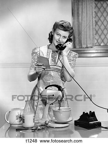 1940 1940S Woman In Kitchen Wearing Apron Holding Recipe Baking Talking On Telephone View Large Photo Image Stock Photo - 1940 1940S Woman In Kitchen Wearing Apron Holding Recipe Baking Talking On Telephone . Fotosearch