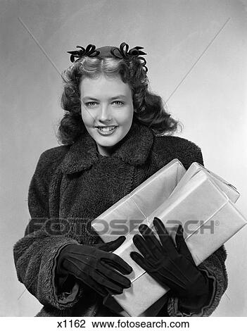 1940 1940S Young Woman Wearing Coat And Gloves And Bows In Her Hair Carrying Wrapped Presents View Large Photo Image Stock Image - 1940 1940S Young Woman Wearing Coat And Gloves And Bows In Her Hair Carrying Wrapped Presents . Fotosearch
