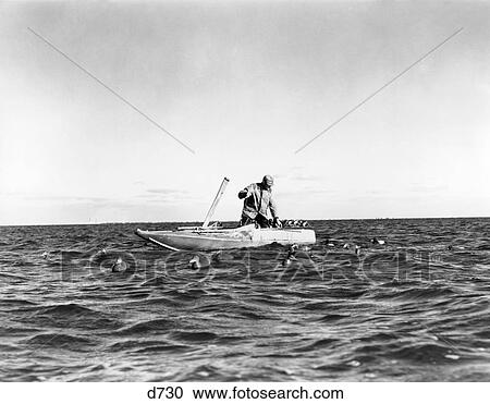 Stock Image - 1940S 1930S Single Man Hunter Small Boat Deploying Duck Decoys Water . Fotosearch