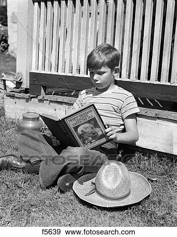 Stock Photo - 1940S Boy In Jeans & Striped T-Shirt Leaning Against Porch Reading The Book Twenty Thousand Leagues Under The Sea . Fotosearch