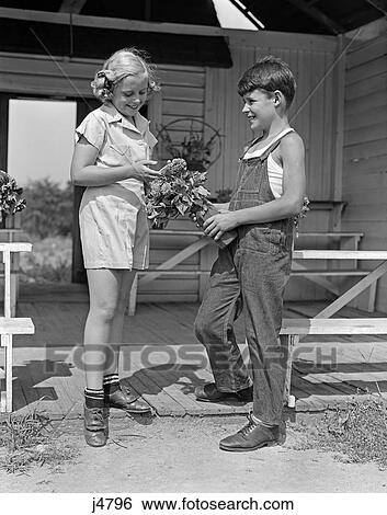 Stock Photograph - 1940S Boy Wearing Overalls Giving Girl Bouquet Flowers At Farm Stand . Fotosearch