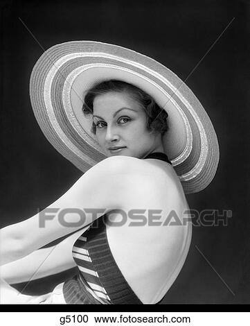 Stock Image - 1940S Closed Mouth Smiling Woman Wearing A Striped Halter Top & Wide Round Striped Straw Hat Looking Over Her Bare Shoulders . Fotosearch