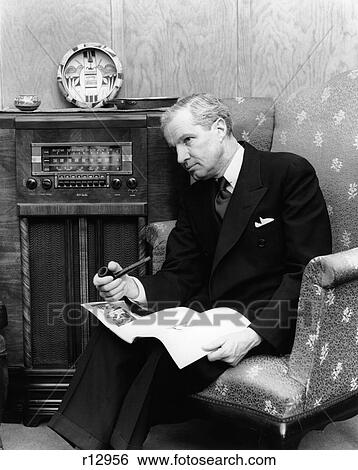 Stock Photograph - 1940S Elderly Man Leaning Head Toward Radio Pipe In Hand & Newspaper In Lap . Fotosearch
