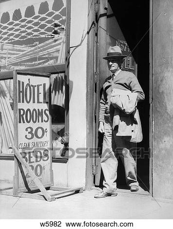 Stock Image - 1940S Elderly Man Walking Out Of Door Next To Sign Reading Hotel Rooms 30 Cents Clean Sanitary Beds 20 Cents . Fotosearch