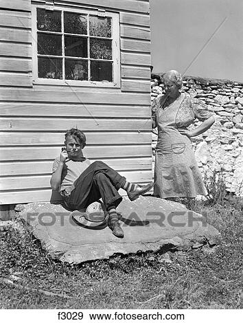 1940S Farm Boy Leaning Against House Smoking Pipe With Grandmother Looking Around Corner At Him With Hand On Hip View Large Photo Image Stock Photo - 1940S Farm Boy Leaning Against House Smoking Pipe With Grandmother Looking Around Corner At Him With Hand On Hip . Fotosearch