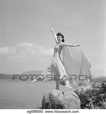 Stock Image - 1940S Female Dancer By Lake In Flimsy Costume Standing On Rock Arms Back. Fotosearch