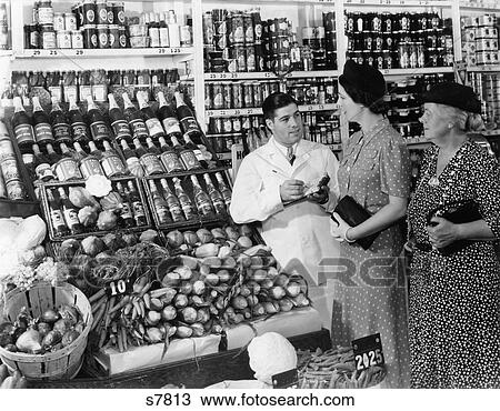 1940S Grocer In White Coat Holding Pad & Pencil To Take Down Orders From Two Women Talking To Him View Large Photo Image Stock Image - 1940S Grocer In White Coat Holding Pad & Pencil To Take Down Orders From Two Women Talking To Him . Fotosearch