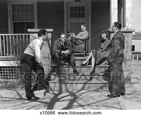 Stock Photograph - 1940S Group Of Five Men & Women Gathered On & Around Front Porch Four In Front Talking Elderly Man In Background Reading Paper. Fotosearch