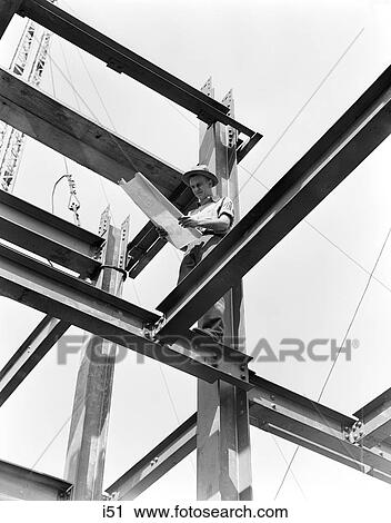 1940S Man In Dress Hat & Work Shirt Holding Blue Print With Both Hands While Standing On Steel Framework Of A Large Building View Large Photo Image Stock Image - 1940S Man In Dress Hat & Work Shirt Holding Blue Print With Both Hands While Standing On Steel Framework Of A Large Building. Fotosearch