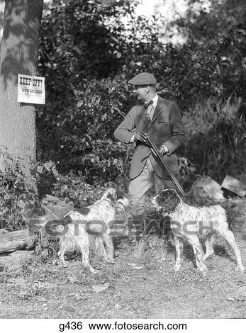 1940S Man With Two Dogs Holding Rifle Reading Sign On Tree Saying Keep Off Hunting Fashion Tresspassing Cap View Large Photo Image Stock Photograph - 1940S Man With Two Dogs Holding Rifle Reading Sign On Tree Saying Keep Off Hunting Fashion Tresspassing Cap . Fotosearch