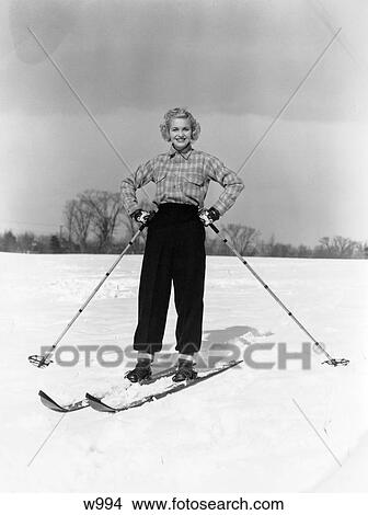 1940S Smiling Blonde Woman On Skis Both Hands On Hips Holding Ski Poles In Snow Field With Tree Background Mittens View Large Photo Image Picture - 1940S Smiling Blonde Woman On Skis Both Hands On Hips Holding Ski Poles In Snow Field With Tree Background Mittens. Fotosearch