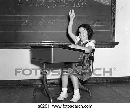 Stock Image - 1940S Smiling Girl Sitting At Desk Raising Her Hand Volunteer Ask Answer Question Blackboard Chalk . Fotosearch