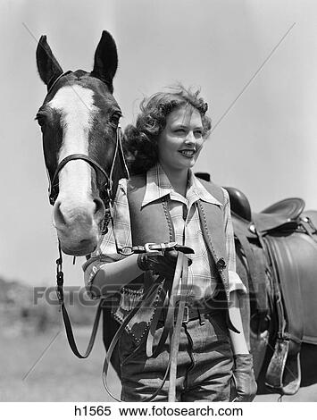 Stock Photography - 1940S Smiling Teen Girl In Studded Fringed Vest Wearing Leather Gloves Holding Reins Of Horse Beside Her . Fotosearch
