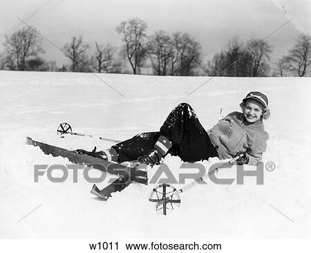 Stock Image - 1940S Smiling Woman In Ski Clothes And Cap Laying In Snow With Skis And Poles Fall Fallen Accident Beginner . Fotosearch
