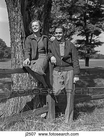 1940S Teen Couple Boy Girl Happy Smiling Full Length Portrait By Wooden Fence And Tree View Large Photo Image Stock Photo - 1940S Teen Couple Boy Girl Happy Smiling Full Length Portrait By Wooden Fence And Tree . Fotosearch