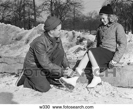 1940S Teen Couple In Knit Caps & Winter Jackets Kneeling Boy Tying Sitting Girls Ice Skates Smiling Romance Innocence Wholesome View Large Photo Image Stock Image - 1940S Teen Couple In Knit Caps & Winter Jackets Kneeling Boy Tying Sitting Girls Ice Skates Smiling Romance Innocence Wholesome. Fotosearch