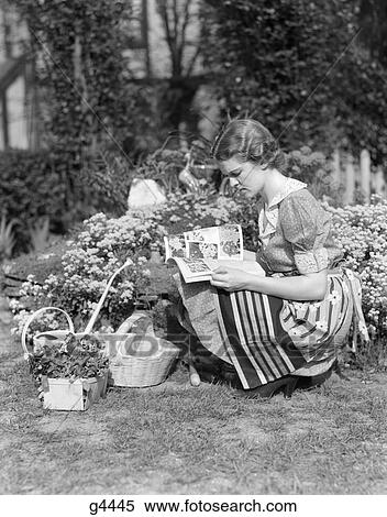 1940S Woman Dressed In Print Dress And Striped Apron Kneeling In Flowers Garden Reading A Gardening Manual Or Magazine View Large Photo Image Stock Photography - 1940S Woman Dressed In Print Dress And Striped Apron Kneeling In Flowers Garden Reading A Gardening Manual Or Magazine . Fotosearch
