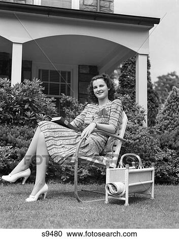 1940S Woman Holding Book Smiling At Camera Sitting In Lawn Chair Magazine Rack Porch House View Large Photo Image Stock Image - 1940S Woman Holding Book Smiling At Camera Sitting In Lawn Chair Magazine Rack Porch House . Fotosearch
