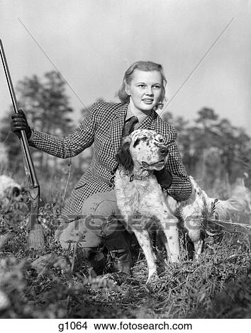 1940S Woman Holding Rifle In One Hand Petting Dog With Other Kneeling In Grass Wearing Tweed Suit View Large Photo Image Picture - 1940S Woman Holding Rifle In One Hand Petting Dog With Other Kneeling In Grass Wearing Tweed Suit . Fotosearch