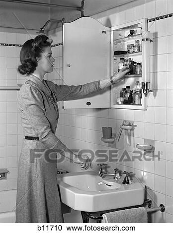 Stock Image - 1940S Woman Reaching Into Medicine Cabinet In Bathroom . Fotosearch