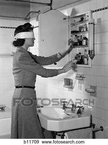 Stock Photo - 1940S Woman Wear Blindfold Reaching Into Medicine Cabinet In Bathroom . Fotosearch