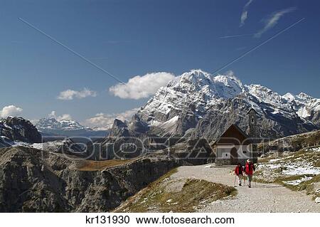 Stock Image - Hikers Trailside Chapel Parco Naturale Dolomiti Di Sesto Italian Alps North Of Cortina D'Ampezzo. Fotosearch