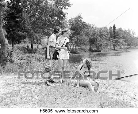 Stock Photography - Three Young Ladies Women Woods Lake Sitting Nature Camera Photographer Photography 1940S Retro. Fotosearch