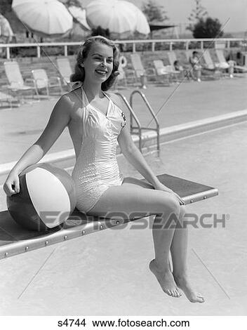 1950 1950S Bathing Beauty In Satin One Piece Sitting On Diving Board With Legs Hanging Off Holding Beach Ball At Side View Large Photo Image Picture - 1950 1950S Bathing Beauty In Satin One Piece Sitting On Diving Board With Legs Hanging Off Holding Beach Ball At Side . Fotosearch