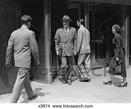 Picture - 1950 1950S Business Man In Suit Carrying Briefcase Leavong Building Men And Woman Entering . Fotosearch