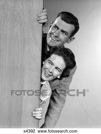 Stock Image - 1950 1950S Couple Looking Out From Behind Door . Fotosearch