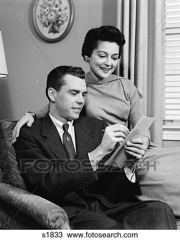 1950 1950S Couple Sitting On Chair Looking At Paper View Large Photo Image Stock Image - 1950 1950S Couple Sitting On Chair Looking At Paper . Fotosearch