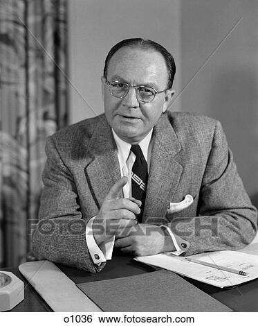 1950 1950S Man In Office Wearing Glasses Sitting At Desk Pointing Finger View Large Photo Image Stock Photograph - 1950 1950S Man In Office Wearing Glasses Sitting At Desk Pointing Finger . Fotosearch