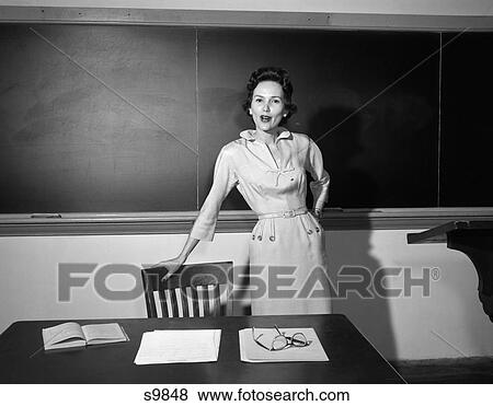 1950 1950S School Teacher Standing In Front Of Board Leaning On Chair By Desk View Large Photo Image Stock Photo - 1950 1950S School Teacher Standing In Front Of Board Leaning On Chair By Desk . Fotosearch