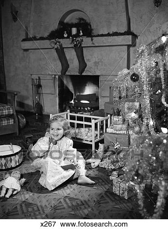 Stock Photo - 1950 1950S Smiling Little Girl Christmas Tree Talking Toy Telephone Toys Doll Crib Fireplace Stockings. Fotosearch