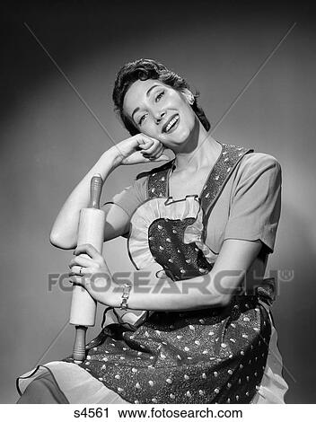 Stock Image - 1950 1950S Woman As Housewife Wearing Apron Holding Rolling Pin . Fotosearch