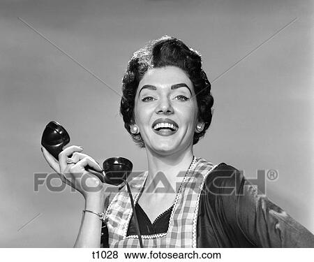 1950 1950S Woman In Apron Holding Telephone Receiver In Hand Away From Ear Looking At Camera Smiling View Large Photo Image Stock Photo - 1950 1950S Woman In Apron Holding Telephone Receiver In Hand Away From Ear Looking At Camera Smiling . Fotosearch