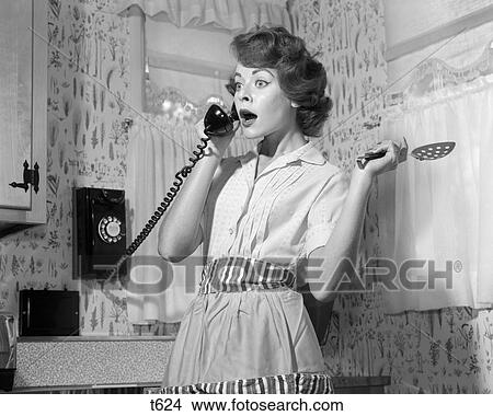 1950 1950S Woman In Kitchen Wearing Apron Holding Spoon Talking On Telephone View Large Photo Image Picture - 1950 1950S Woman In Kitchen Wearing Apron Holding Spoon Talking On Telephone . Fotosearch