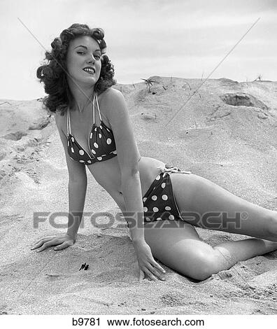 1950s ブルネット 水着美人 伸ばされる 中に 砂 身に着けていること ポルカドット ビキニ ストックイメージ B9781 Fotosearch