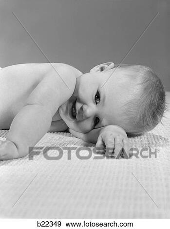 Stock Photo - 1950S 10 Month Old Baby Laying On Bed With Head Turned To One Side Smiling . Fotosearch